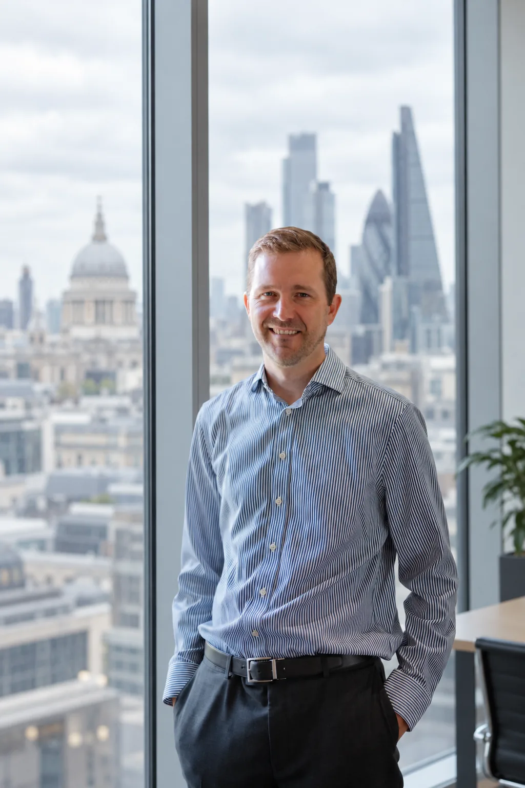 Nat Baldwin standing by a floor-to-ceiling window overlooking the City of London